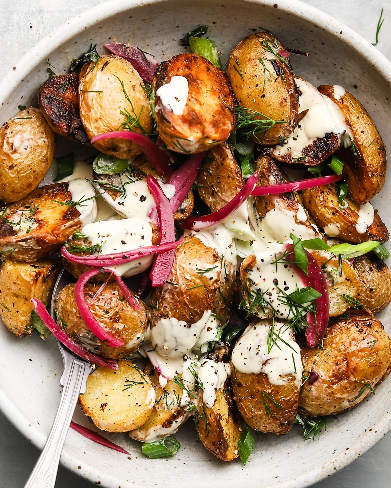 Grilled potato salad with horseradish sauce, garnished with herbs and pickled onions.