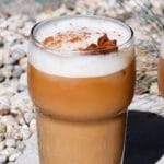 Frothy iced chai latte with cinnamon and star anise garnish in a glass.