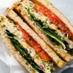 Sandwich with chickpea salad, fresh greens, tomato, and sprouts, on toasted bread.