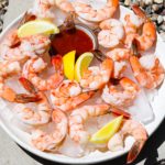 A plate of shrimp cocktail with lemon wedges and cocktail sauce on ice.