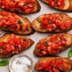 Slices of toasted bread topped with diced tomato bruschetta, garnished with basil leaves.
