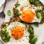 Two fried eggs with pesto on toast, seasoned with chili flakes and pepper.