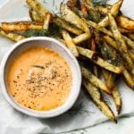 Crispy fries with dill and creamy orange dip on a plate.
