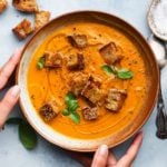 Creamy heirloom tomato soup with sesame croutons and basil garnish in a bowl.