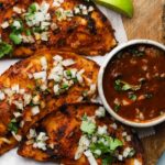Grilled birria tacos with onions and cilantro, served alongside a bowl of sauce.