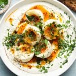 Eggs with chili butter and yogurt garnished with fresh herbs in a bowl.