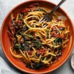 A bowl of pasta with sun-dried tomatoes, spinach, mushrooms, and grated cheese.