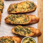 Sliced garlic bread topped with herbs and Calabrian chili on parchment paper.