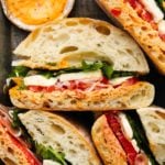 Sliced sandwiches with prosciutto, mozzarella, tomatoes, and greens on crusty bread with chili spread.