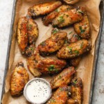Crispy lemon pepper wings on parchment with a side of creamy dipping sauce.