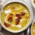 Creamy broccolini and cheddar soup topped with crispy prosciutto in a bowl.