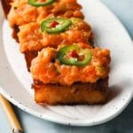 Spicy salmon on crispy rice, topped with jalapeño slices on a white plate.