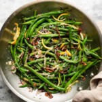 Green beans with lemon slices, crispy shallots, and shredded cheese in a skillet.