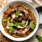 Bowl of Kashke Bademjan garnished with caramelized onions and fresh mint leaves.