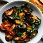 Mussels in spicy tomato sauce topped with fresh herbs and served with bread.