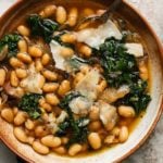A bowl of brothy beans with greens and shaved cheese on top.