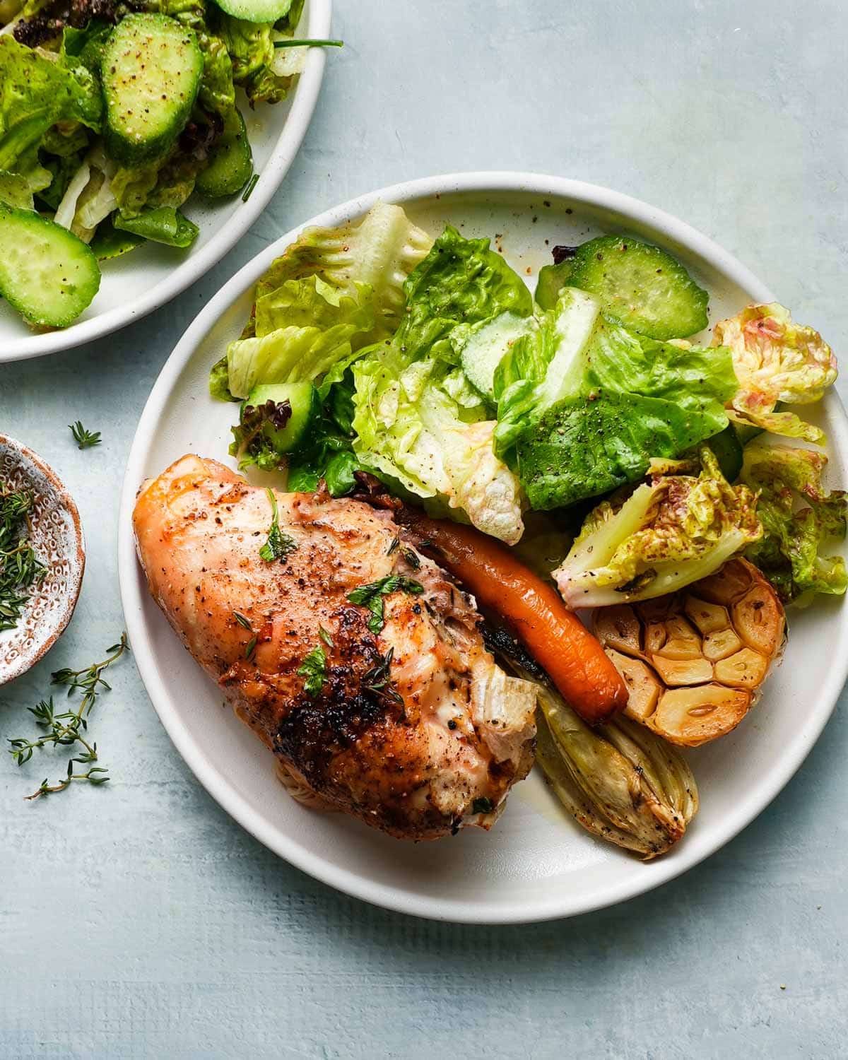 Roasted chicken breast with garlic, salad, and vegetables on a white plate.