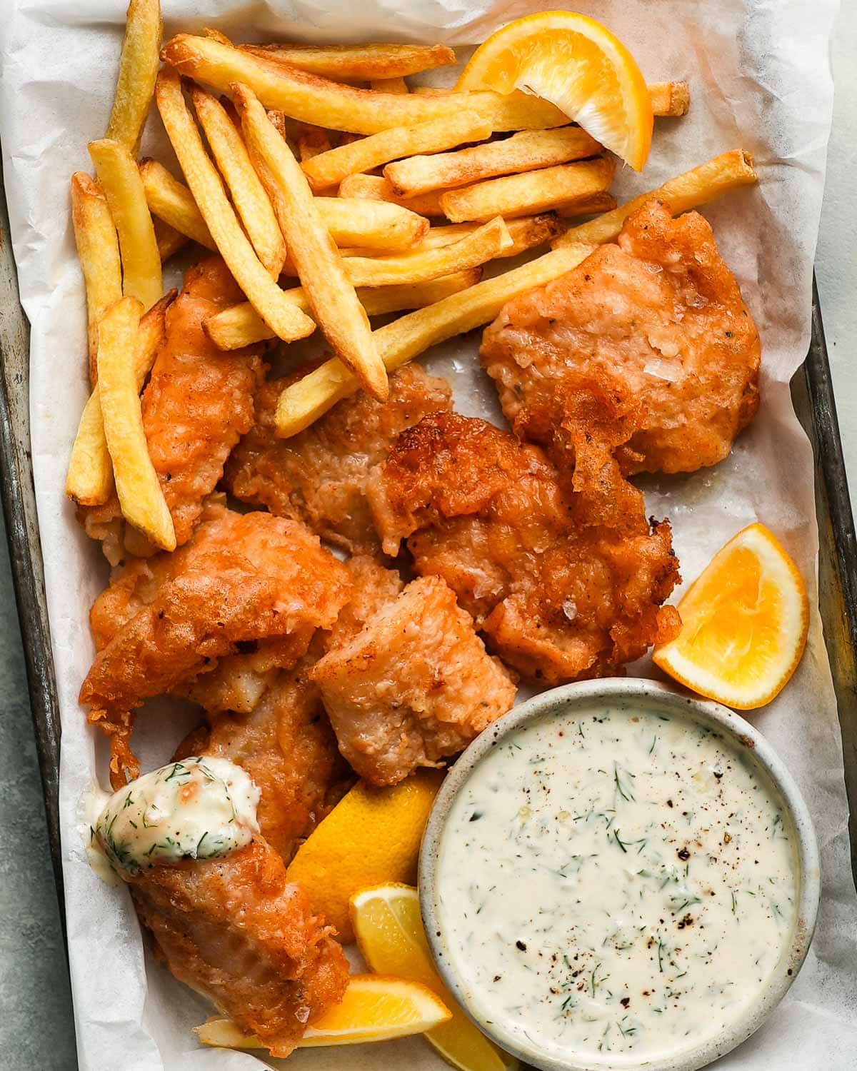 Fried cod with fries, lemon wedges, and tartar sauce on a tray.