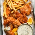 Crispy battered cod with fries, tartar sauce, and lemon wedges on a tray.