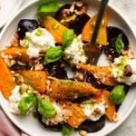 Colorful beet and burrata salad with hazelnuts and fresh basil on a white plate.