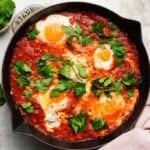 Shakshuka dish with poached eggs in tomato sauce, garnished with fresh parsley.