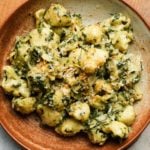 Creamy pasta with spinach, artichoke, and cheese, garnished with breadcrumbs in a bowl.