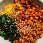 Sweet potato, kale, couscous, chickpeas, and sunflower seeds in a colorful bowl.