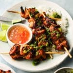 Grilled chicken skewers with green herbs, rice, lime wedges, and dipping sauce.