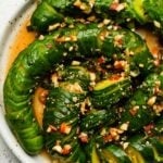 Sliced cucumber salad with chili, garlic, and sesame seeds on a white plate.