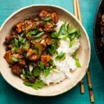 Tofu and celery stir-fry with rice, garnished with green onions and sesame seeds.