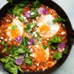 Skillet huevos rancheros topped with fried eggs, cilantro, radishes, and crumbled cheese.