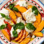 Fresh peach and burrata salad with basil, in a decorative bowl.