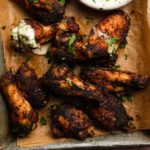 Charred chicken wings with herbs and creamy chive dip on parchment paper.