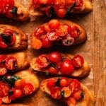 Slices of toasted bread topped with cherry tomatoes and fresh basil.