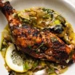 Grilled chicken leg with lemon and charred leek sauce in a white bowl.