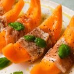 Slices of melon wrapped in prosciutto, garnished with basil and cracked pepper.