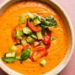 Creamy orange gazpacho topped with diced cucumbers, tomatoes, and fresh basil leaves.