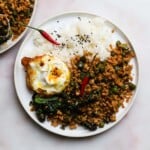 Plate of Thai basil chicken, rice, fried egg, and red chili on a plate.
