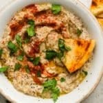 Bowl of baba ganoush with paprika, parsley, and pita bread.