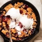Skillet mixed berry cobbler topped with melting ice cream and a spoon.