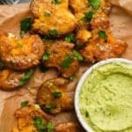 Crispy smashed potatoes with fresh herbs and creamy green dip in a bowl.