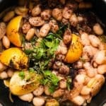 Braised butter beans with lemon, sumac, and fresh herbs in a black dish.