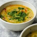 Bowl of creamy potato leek soup garnished with chopped herbs and spices.
