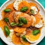 Slices of persimmon and mozzarella with basil on a white plate.