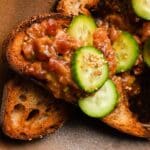 Tuna tartare on toast topped with cucumber slices and sesame seeds.
