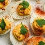 Deviled eggs topped with parsley and sprinkled with paprika and black pepper.