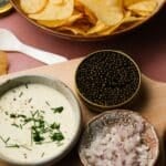 Bowl of potato chips with caviar, cream sauce, and chopped onions on the side.