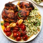 Grilled chicken thighs with couscous salad and roasted cherry tomatoes on a plate.