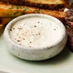 Small bowl of horseradish cream sauce with herbs and seasonings on top.