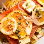Salmon topped with sliced citrus, capers, shallots, and butter, seasoned with spices.